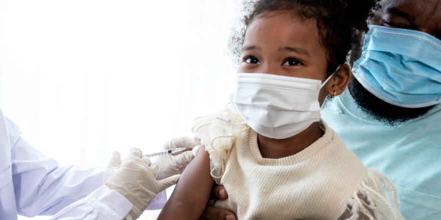 A 5-year-old African-American girl, wearing a surgical mask, whose father was vaccinated for prevent virus from COVID-19 and flu, to people health care and vaccine concept.